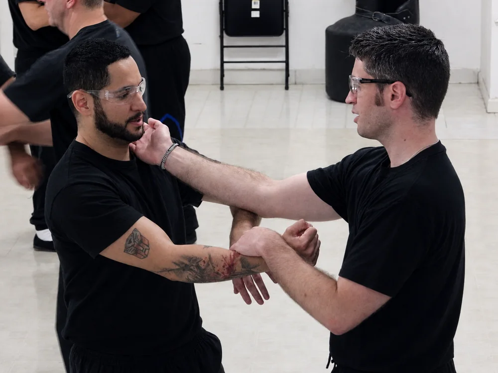 Two students in black training clothes working a close-range arm bridge in class
