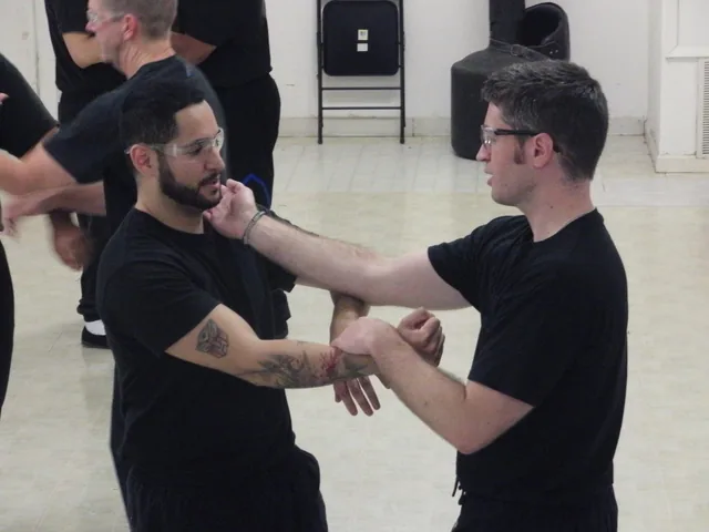 Two students in black training clothes working a close-range arm bridge in class