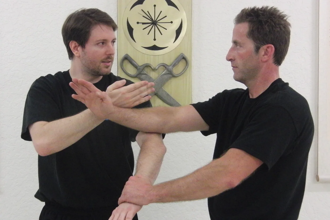 Two students practising Chi Sau at Dragon Martial Arts, in front of the school's plum-blossom plaque and butterfly swords